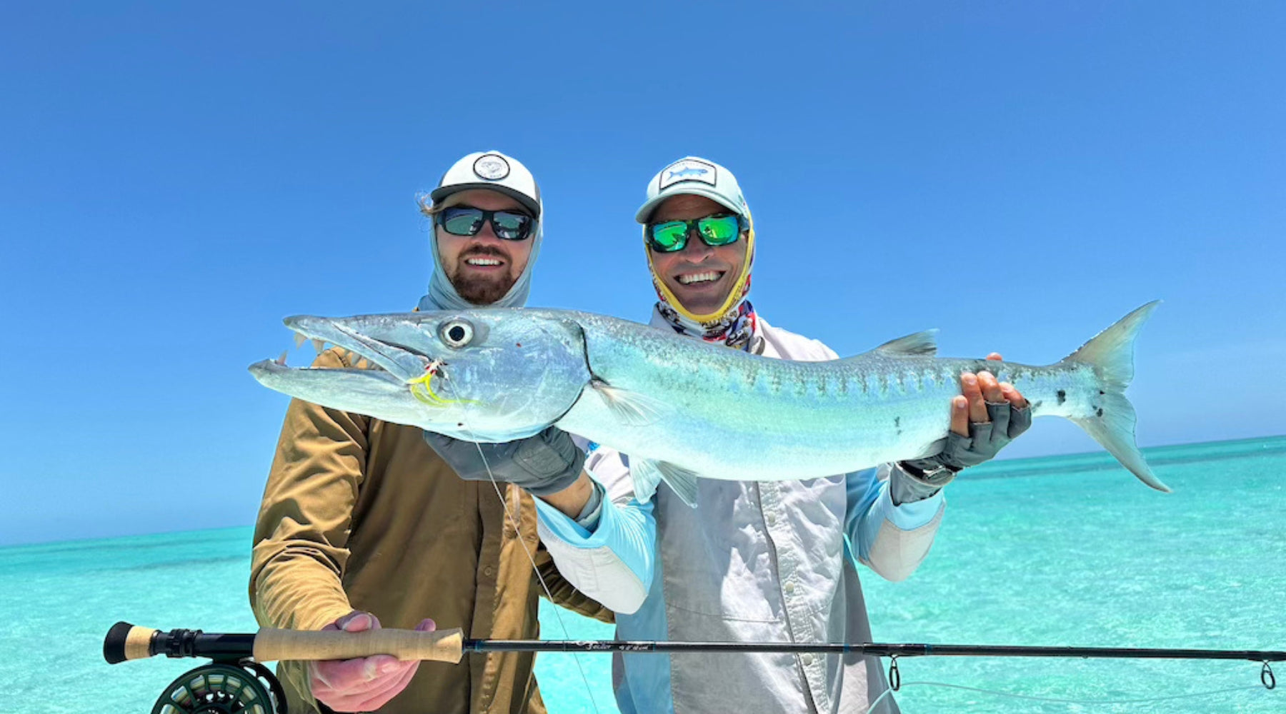 two men hold a large barracuda while fly fishing in cuba